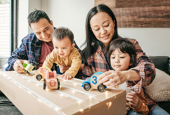 Two adults and two children playing with toy cars on a coffee table lighted with LED's, breathing easy thanks to their Aprilaire purifier