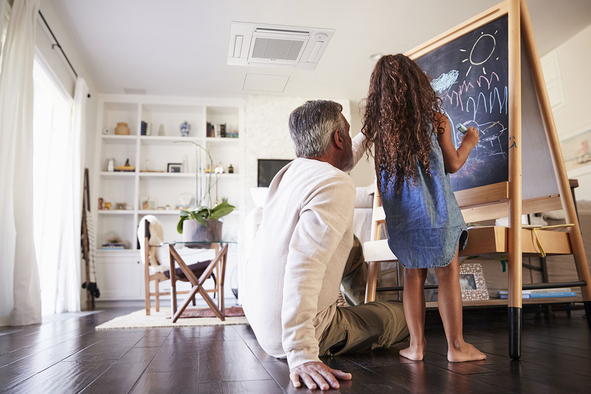 Man sitting next to young girl at a chalkboard easel, ductless mini split cooling and heating system in the ceiling