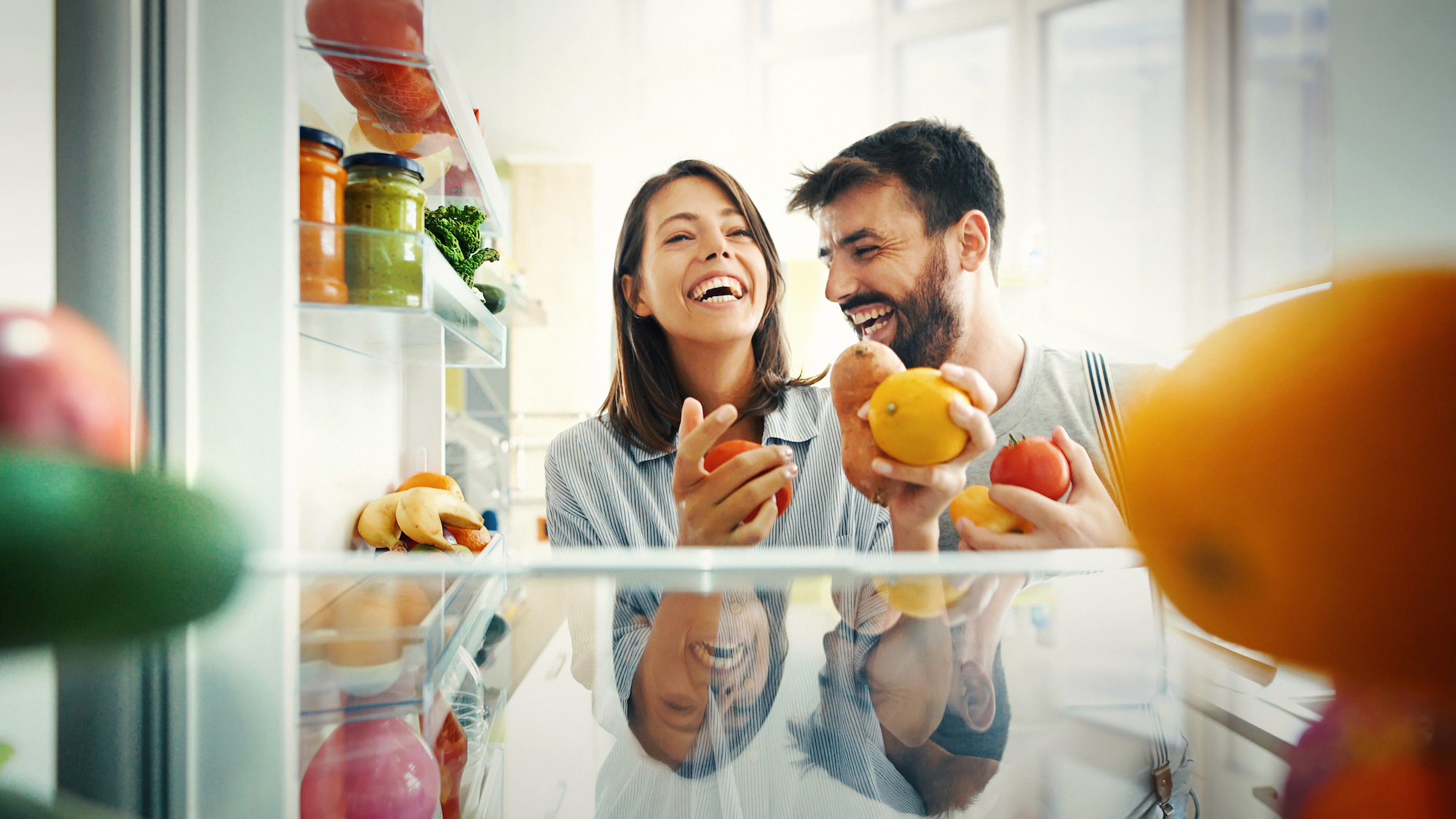 Man and woman laughing while picking fruits and veggies from the fridge, enjoying their air purification system