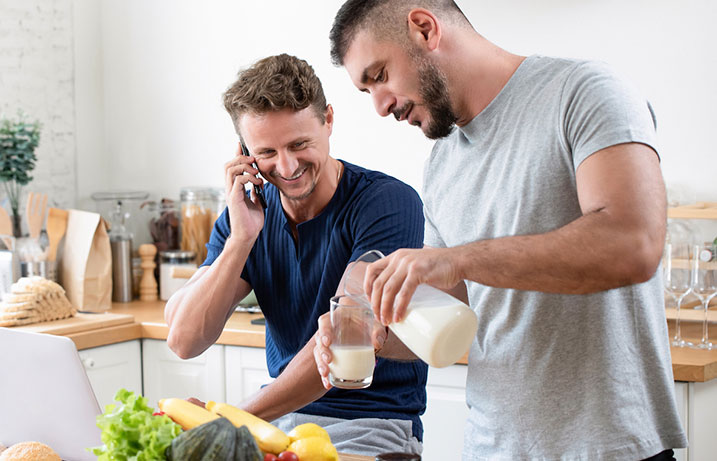 Man smiling on the phone about the rebate he earned by choosing a ductless system overlooking another man pouring some milk