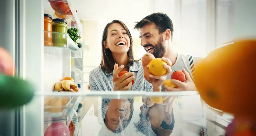 Man and woman laughing while picking fruits and veggies from the fridge, enjoying their air purification system