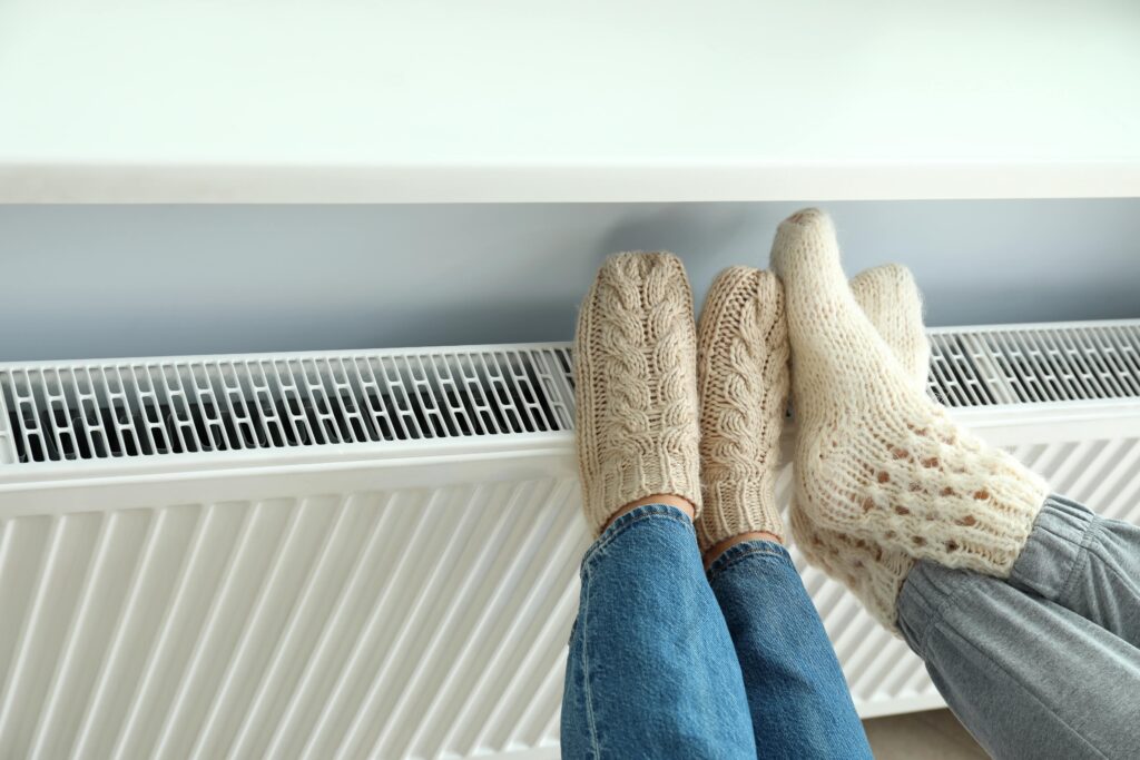 Two people wearing knitted socks rest their feet on a white radiator.