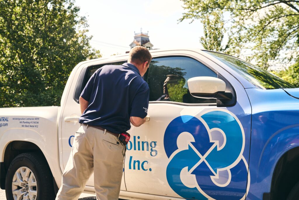 A man in a blue shirt stands next to a branded Brookline HVAC truck, looking into the driver’s side window on a sunny day.