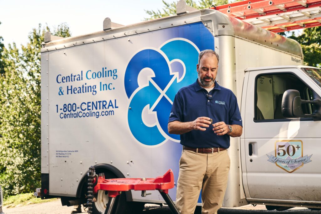 A man in a blue shirt stands in front of a Central Cooling & Heating Inc. service truck parked outdoors in Burlington.