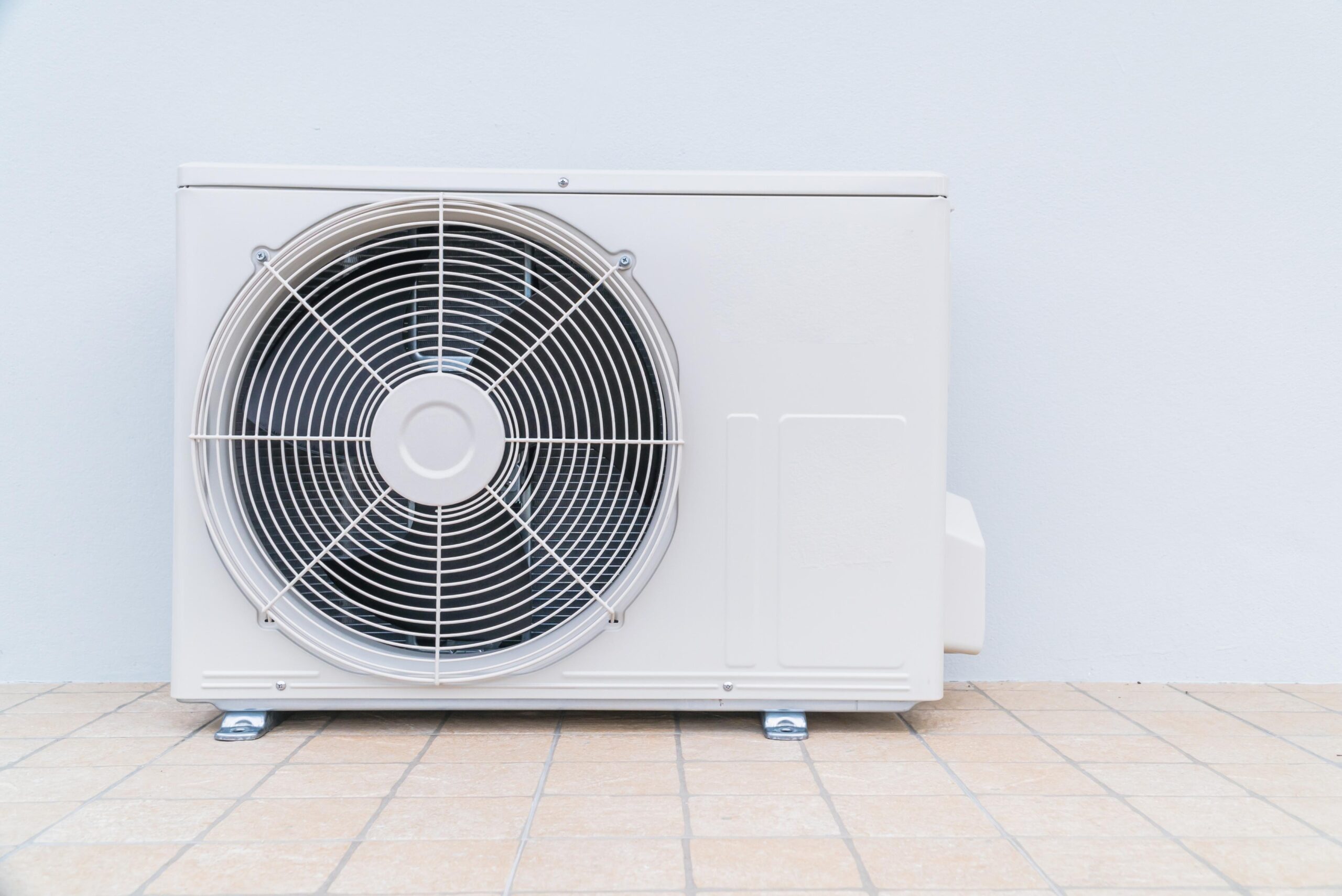A white outdoor air conditioning unit, installed on a tiled floor against a plain light-colored wall, showcases professional AC installation North Shore expertise by Central Cooling & Heating.
