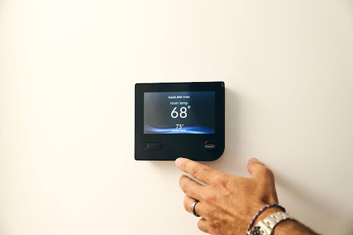 A hand adjusts a digital thermostat mounted on a white wall, displaying an indoor temperature of 68 degrees Fahrenheit—a common scene when comparing central air vs ductless systems.