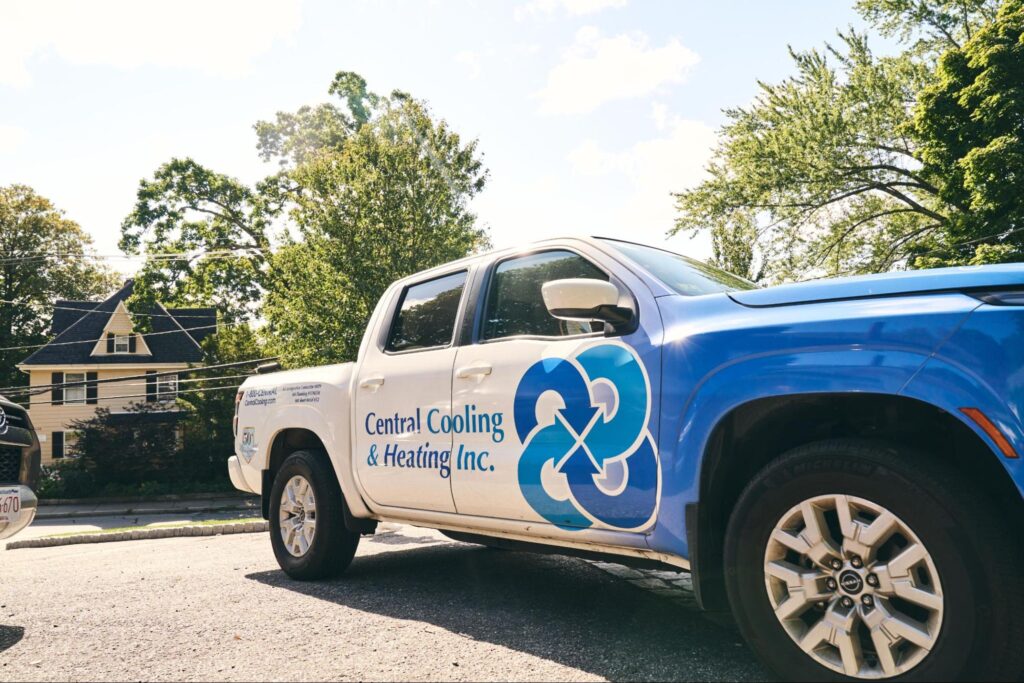 A blue and white Central Cooling & Heating Inc. pickup truck, known for its reliable plumbing services, is parked on a residential street with houses and trees in the background.