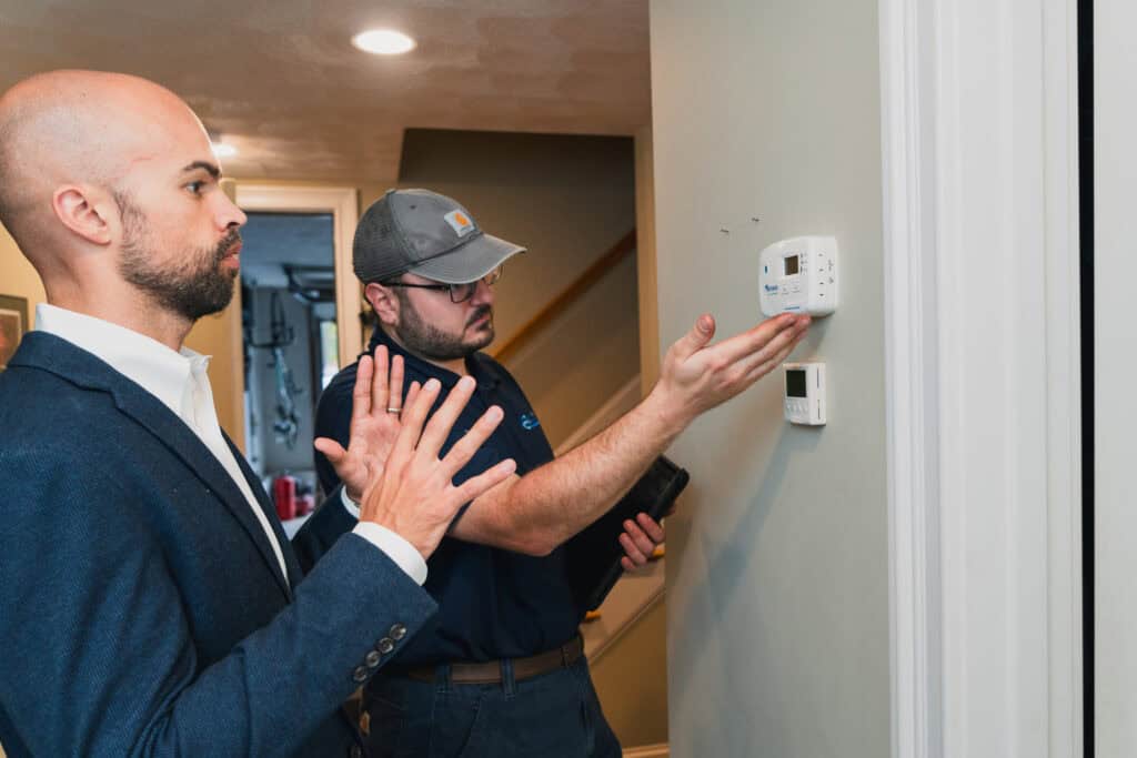 Central Cooling & Heating technician explaining heating system thermostat settings to homeowner indoors