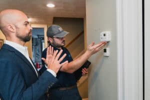 Central Cooling & Heating technician explaining heating system thermostat settings to homeowner indoors