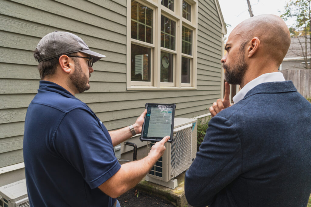 Central Cooling & Heating technician reviewing heat pump system details with homeowner beside outdoor unit