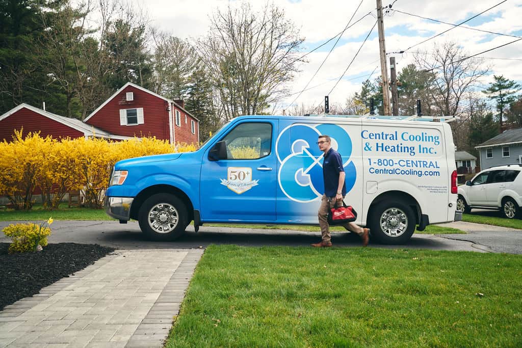 A technician carrying a tool bag walks toward a house from a Central Cooling & Heating Inc. service van parked in a suburban driveway.